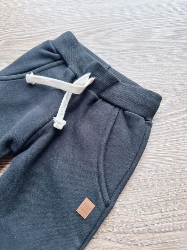 Calça Moletom Peluciada Liso Preto MiniMalista — vista frontal em flatlay, cós elástico wide sem cadarço, interior peluciado macio, algodão premium 100% antialérgico.