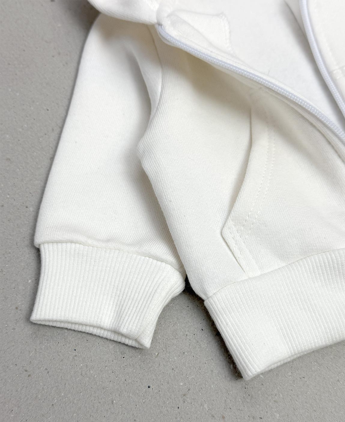 Casaco Moletom Capuz Zíper Peluciado Off-White MiniMalista — vista de costas mostrando o capuz amplo e a barra em ribana ajustada. 100% algodão fio penteado com interior peluciado quentinho, tratamento anti-pilling.