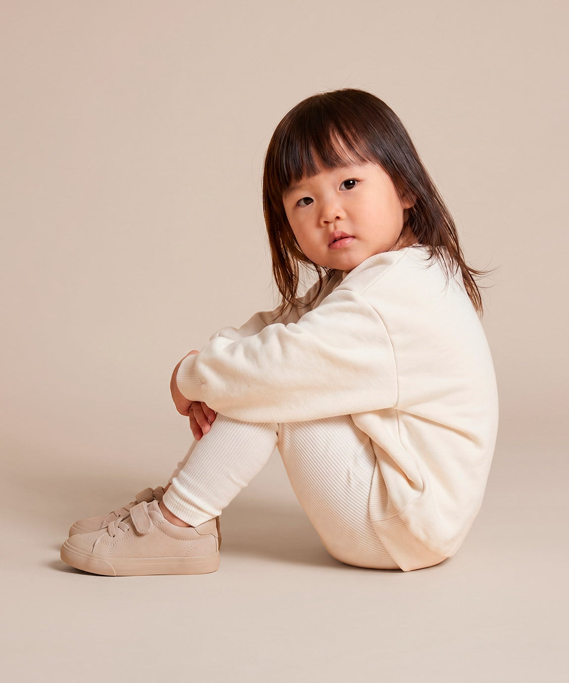 MiniMalista Conjunto Moletom + Calça Canelada Liso Branco Off vestido em criança. Look all-white elegante infantil 100% algodão, moletom peluciado e calça canelada slim no mesmo tom, conjunto unissex menino e menina.