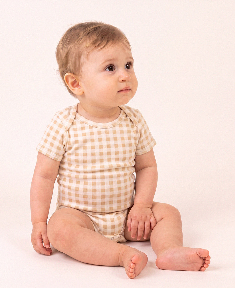 Bebê vestindo o Body Manga Curta Vichy Bege MiniMalista, vista frontal. Body de bebê em algodão com gola americana, xadrez vichy bege, unissex menino e menina.